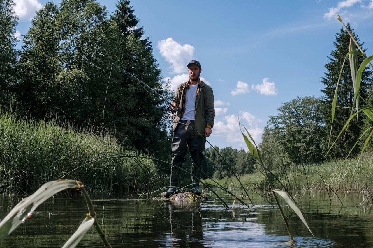 Man in Gray Jacket and Blue Denim Jeans Standing on Brown Wooden Boat on River during